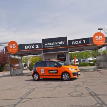 Orangefarbenes Auto mit waschkraft Beschriftung vor einer SB-Autowaschanlage mit zwei Boxen.