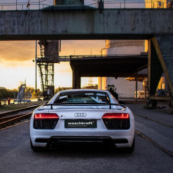 Weißer Audi R8 bei Sonnenuntergang in industrieller Umgebung, mit waschkraft Logo auf dem Nummernschild.
