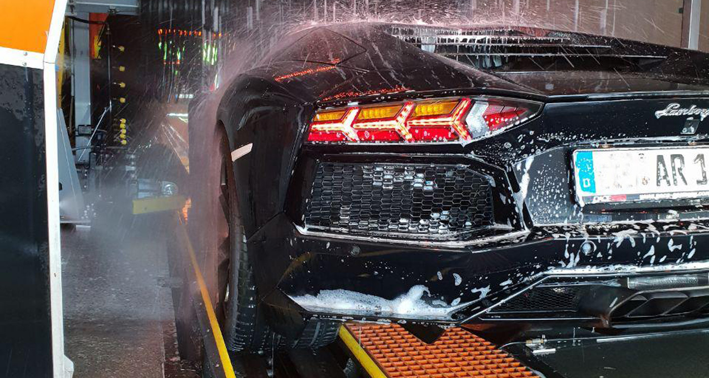 Schwarzer Sportwagen in einer Autowaschanlage, Wasser und Schaum auf dem Lack, leuchtende Rücklichter.