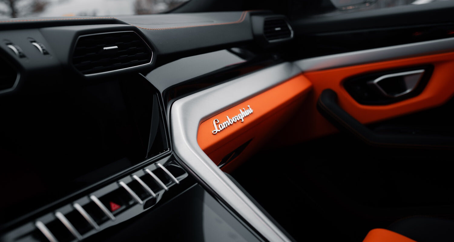 Innenraum eines Autos mit grauem und orangem Armaturenbrett, Marke Lamborghini erkennbar.