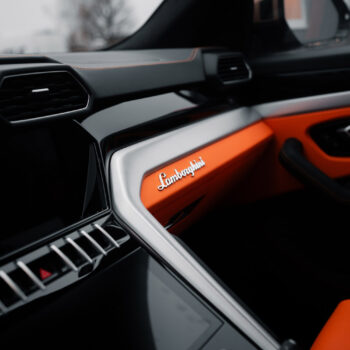 Innenraum eines Autos mit grauem und orangem Armaturenbrett, Marke Lamborghini erkennbar.